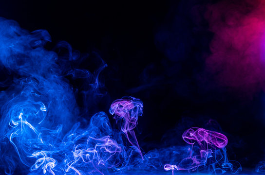 Conceptual image of multi-colored smoke isolated on dark black background, Halloween design element.
