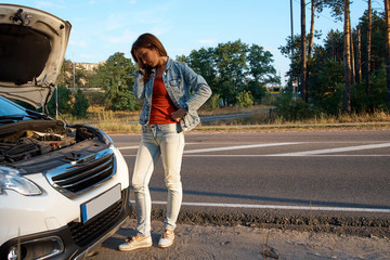 Girl driver next to a broken car with an open hood. Upset, sad girl near the car