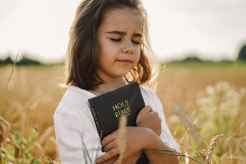 Girl holds bible in her hands. Reading the Holy Bible in a field. Concept for faith, spirituality...