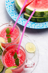 fresh vegetarian watermelon  cocktail in transporant cups on white table with fresh  watermelon,  lime, melissa.