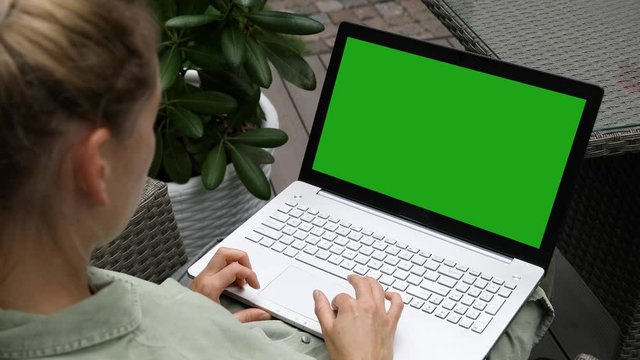 woman using laptop computer on a outdoor terrace, blank green screen copy space