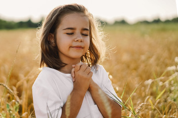 Little Girl closed her eyes, praying in a field wheat. Hands folded in prayer. 