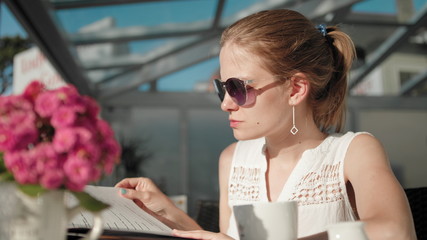 Young Woman with Ponytail and Sunglasses is Drinking Coffee in the Restaurant
