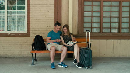 Family Couple is Waiting for Train with Phone and Book. Technology vs Tradition