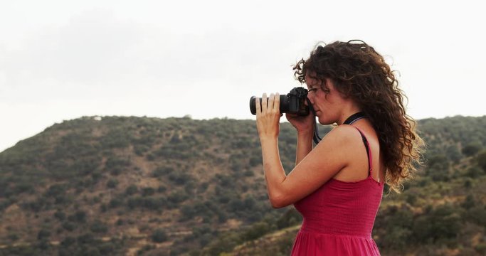 Woman in red dress and a camera photographs nature. Landscape photographer, independent and adventurous woman