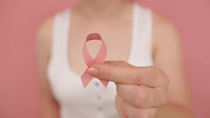Close up, woman holding silk pink ribbon between her fingers. Brest cancer awareness month pink october. High quality photo