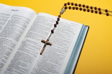 Open Bible in spanish with rosary crucifix on over yellow