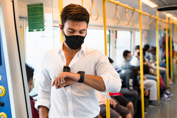 Portrait of a man wearing face mask which looking on his watch standing in the public train.