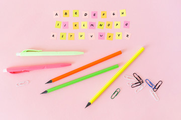 English alphabet completely and school supplies. Multicolored pieces of paper with the abc letters. Pens, pencils and paper clips bright color. Studying of foreign language.