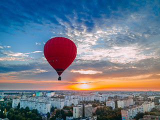 Red hot air balloon flying over small european city at summer sunrise