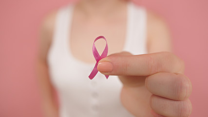 Young woman holding symbolic pink ribbon between her fingers. Breast cancer awareness month, pink october. High quality photo - obrazy, fototapety, plakaty