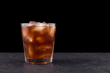 Iced coffee with ice in a transparent misted glass against a dark background with copy space
