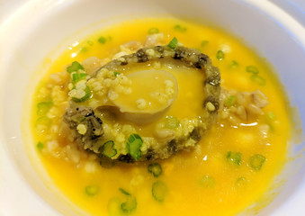 one braised abalone in yellow sauce in white bowl