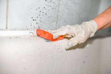 The woman is cleaning the bath. A gloved hand holds a washing sponge. House cleaning. A real dirty bath. Close-up