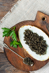 Black caviar. Black sturgeon caviar in a ceramic bowl and in a metal spoon on a wooden serving Board. A healthy treat. Top view with space for text