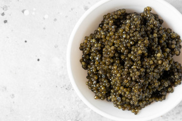 Black caviar. Black sturgeon caviar in a ceramic bowl and a metal spoon on a light background. Useful delicacy. Top view with space for text