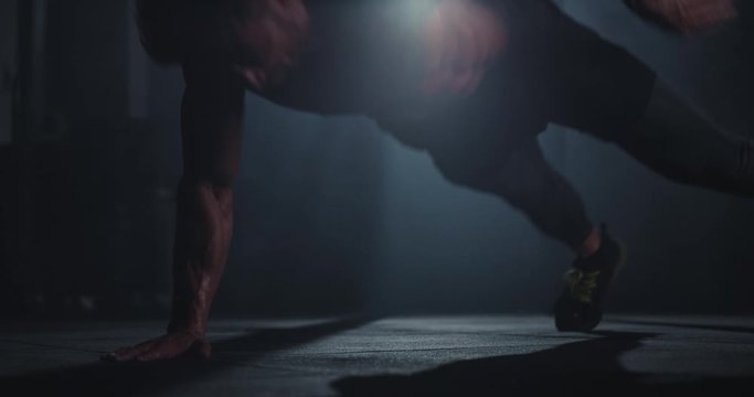 Athletic guy with a strong body doing hard push-ups in a dark cross fitness class training intense