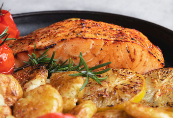 grilled baked salmon fillet with roasted new potatoes , lemon, tomato, close up