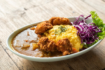 curry rice topped wih fried chicken and scrambled eggs on wooden table