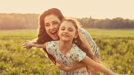 Happy enjoying mother hugging her playful laughing kid girl in sunset sunny light on summer background in bright yellow colors. Closeup
