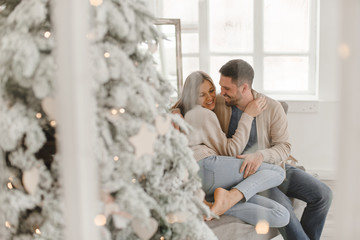Young beautiful happy couple, sitting on the couch near the Christmas tree.