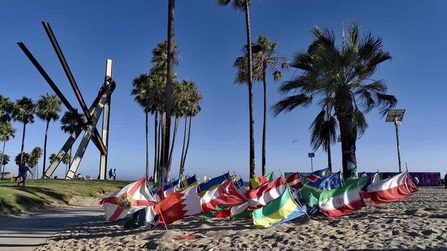 Multiple multi-country Flags waving in a the wind at Venice BEach Boardwalk on windy day with people in background