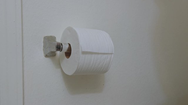 Male hands pulling toilet paper roll and using toilet paper in restroom.