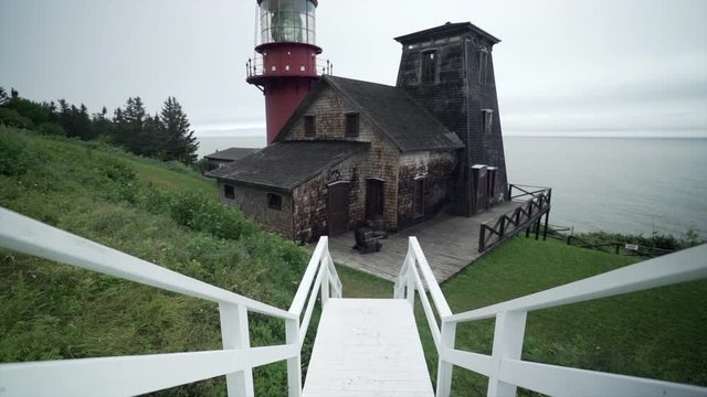Tilting up from Rustic White Country Style Stairs to Reveal a Red Lighthouse and Rustic Country Barn Style Building on the Coast during an Overcast Day