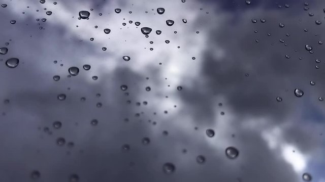 White puffy clouds passing by in the blue sky with sunlight shining through with rain drops on a glass window in focus - HD Time-lapse