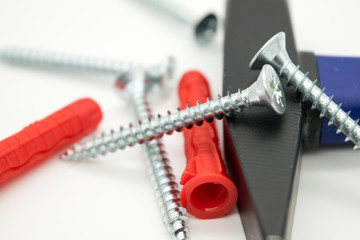 Metal screws, hammer, red dowels on a white background