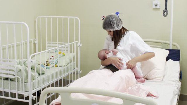 Tracking shot of mother sitting on medical couch in maternity hospital ward and breastfeeding newborn baby