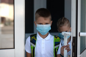 Fototapeta na wymiar Back to school. Schoolchildren come in masks from school doors. Child going school after pandemic over. students are ready for new year.