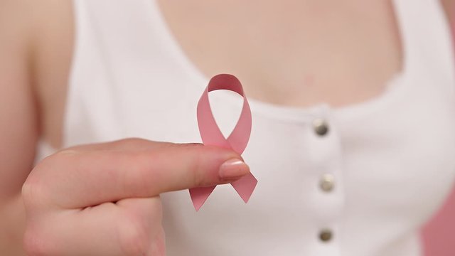 Close up, woman holding symbolic pink ribbon, brest cancer awareness and hope concept. High quality 4k footage