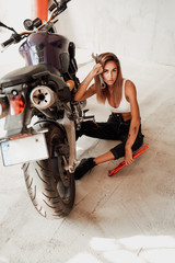 Fototapeta na wymiar An attractive girl in dirt sirring near sport moto bike