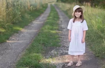 Deurstickers Klein meisje in een hoed en witte jurk staat op een weg in de buurt van roggeveld. © Albert Ziganshin