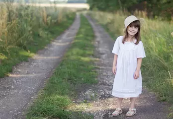 Poster Gelukkig klein meisje in een hoed en witte jurk staat op een weg in de buurt van roggeveld. © Albert Ziganshin