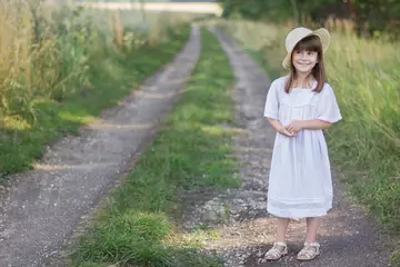Foto op Plexiglas Gelukkig meisje op de weg. Schattig meisje in een witte jurk staat in de buurt van een veld met aartjes van tarwe. © Albert Ziganshin