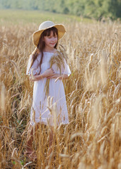 Beautiful girl in a hat stands on a field of rye at sunset