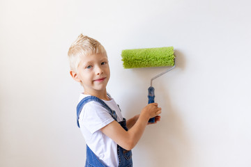 child boy Builder paints white walls with a roller in the apartment, the child makes repairs at home