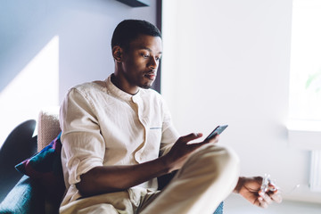 Young African American guy using phone in light room