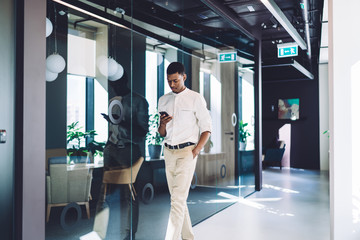 Fototapeta premium Focused ethnic businessman texting smartphone and walking along office hall