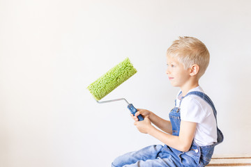 portrait of a child Builder in an apartment with white walls and a roller for painting the walls in his hands, a place for text, repair concept