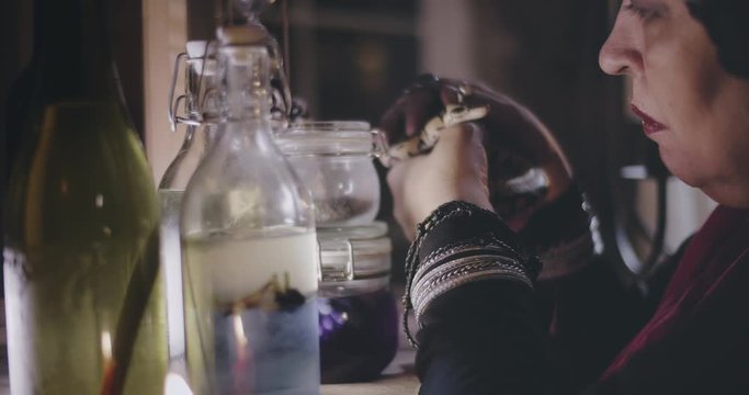 Old witch holding snake and standing near jars with potions