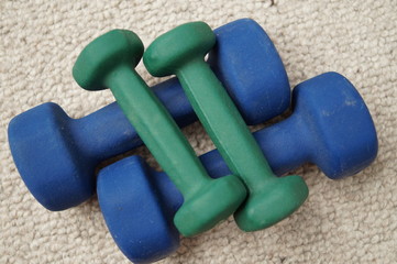 There are two blue dumbbells on the carpet and two smaller green dumbbells on top of them. The view from the top