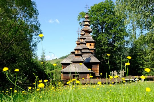 Beautiful historic wooden former lemko church in the village of Kotan on a sunny morning. Yellow flowers in foreground. Low Beskids Mountains, Poland