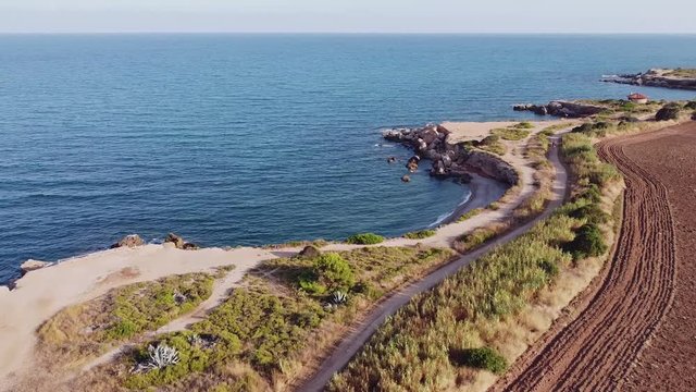 Aerial view of a rocky coastline near a plowed soil field, Jardi de Sol de Riu, Vinaros, Spain.