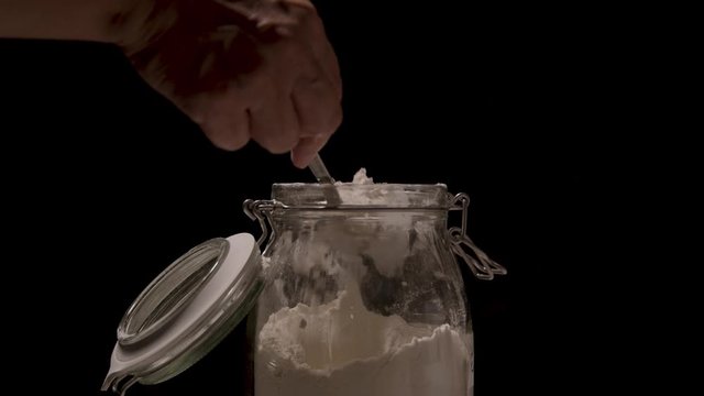 Taking flour from a jar with a tablespoon close up on a black backdrop