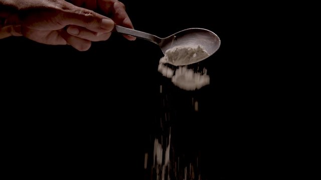 Flour being poured off a tablespoon on a black backdrop