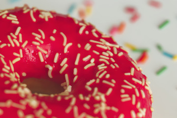 A doughnut covered in red icing and light sprinkles close-up on a light background. Delicious fresh...