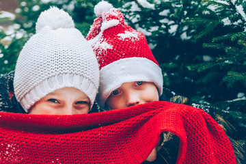 Two European boys in red and white hats playfully look out from under a knitted scarf. holiday of Christmas. Children are happy New year.